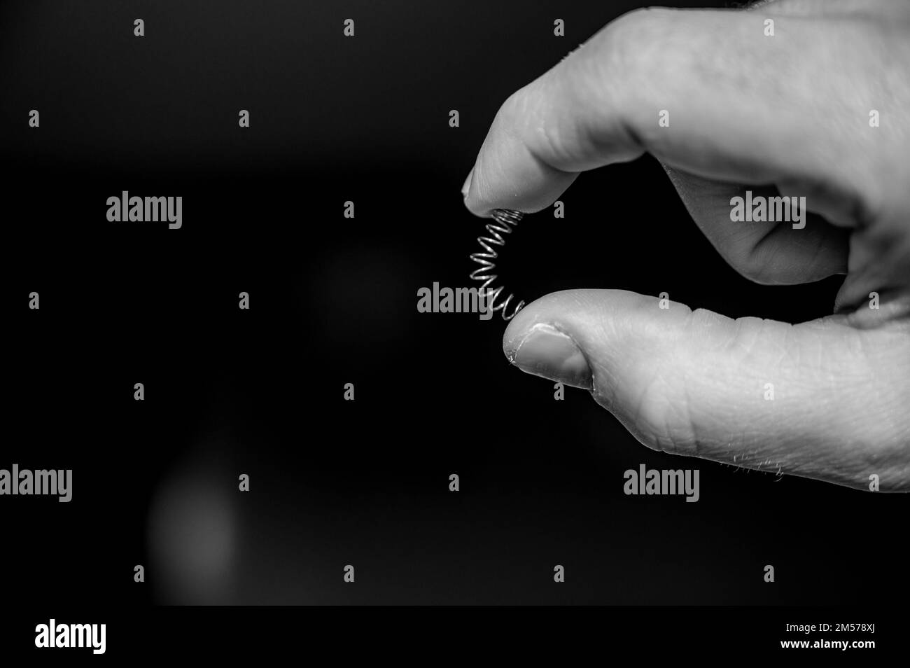 Kaukasische hand Komprimieren einer Metallfeder zwischen Daumen und Finger Stockfoto