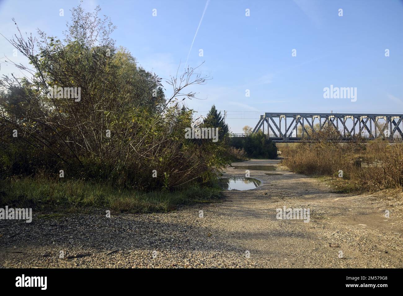 Unbefestigter Pfad mit Pfützen und einer Brücke im Hintergrund auf dem Land Stockfoto