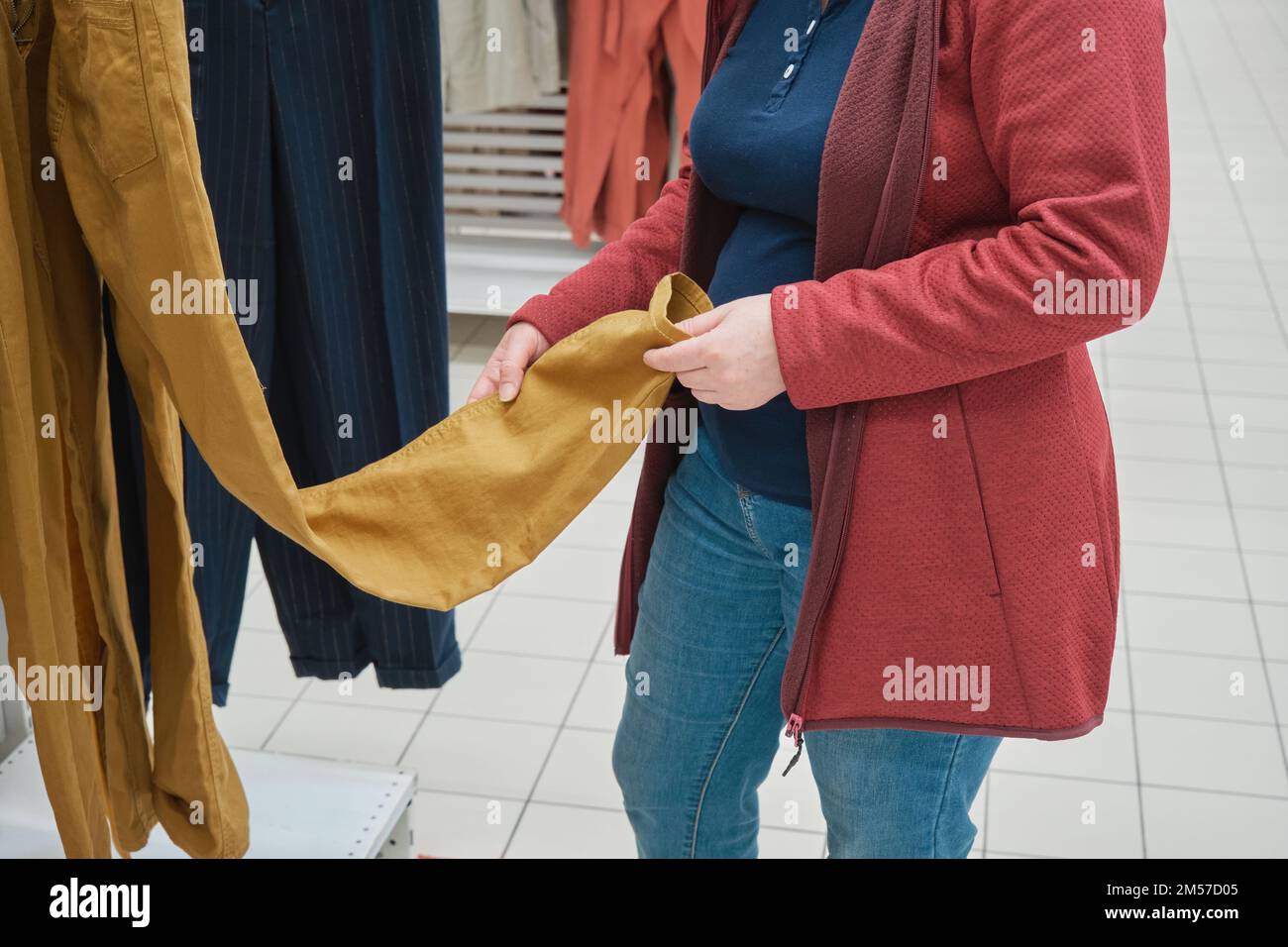 Schwangere Frau wählt lose gelbe Hosen im Geschäft. Hände aus der Nähe Stockfoto