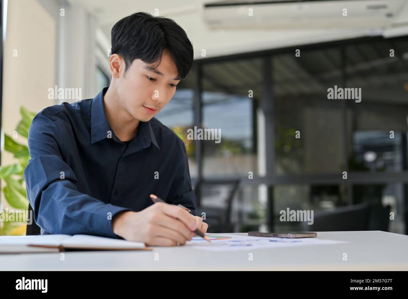 Konzentrierter junger asiatischer Finanzanalyst oder Buchhalter, der an Finanzberichten arbeitet und Finanzdaten auf dem Bericht analysiert. Stockfoto