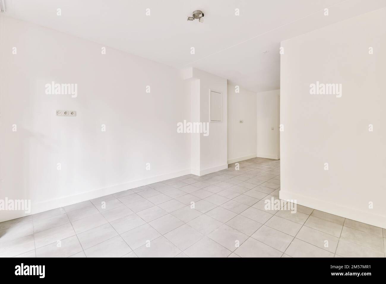 Ein leerer Raum mit Fliesenboden und weißen Wänden, es gibt eine Tür in der Ecke auf der linken Seite Stockfoto