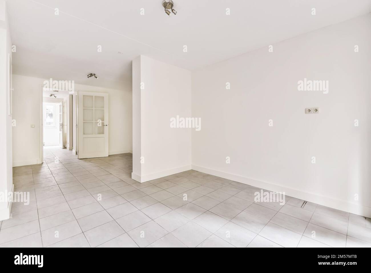 Ein leerer Raum mit Fliesenboden und weißen Wänden, es gibt eine Tür zur linken Seite des Raums Stockfoto