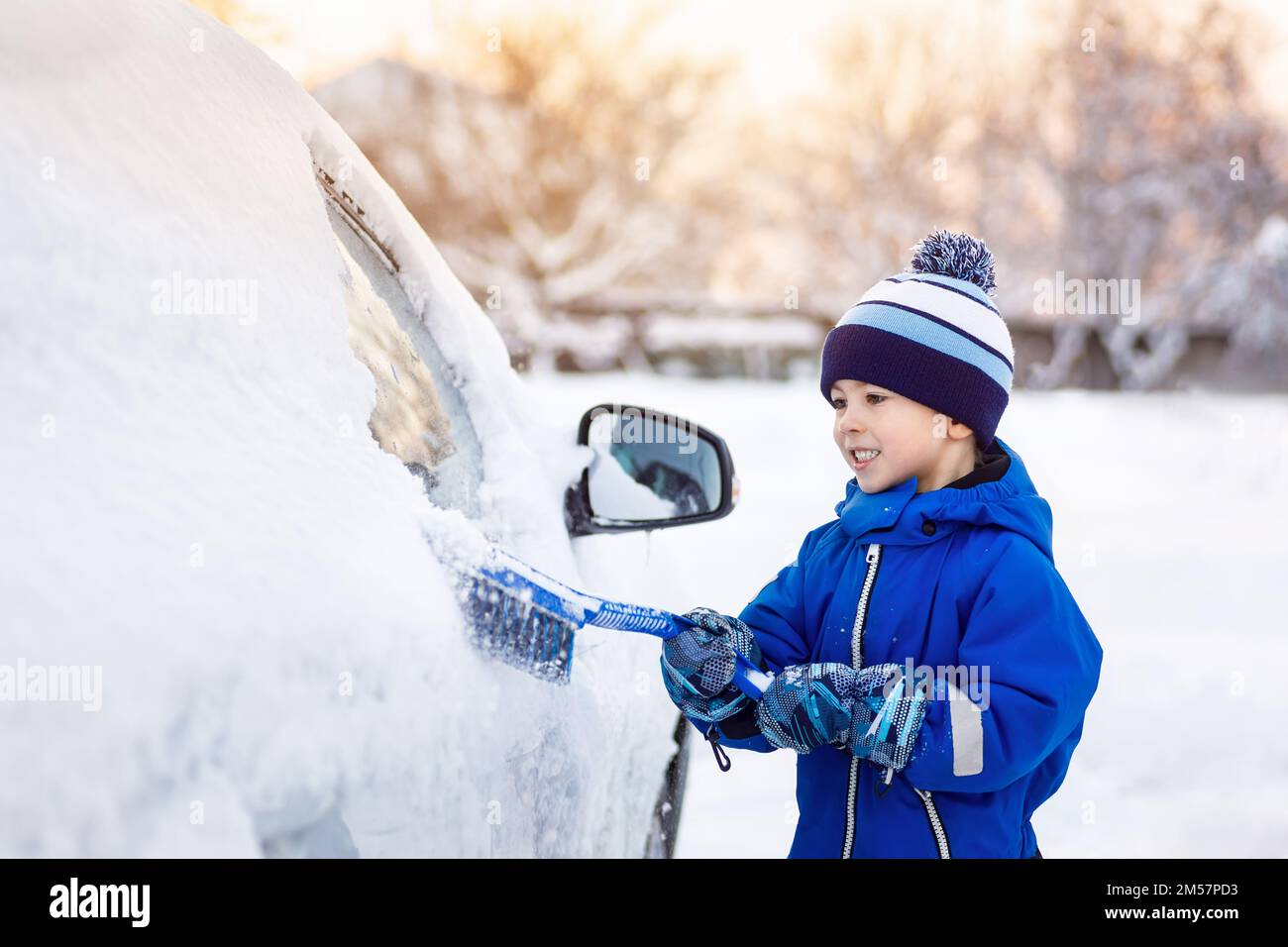 Ein lächelnder Junge, der dabei hilft, den Schnee aus dem Auto des Vaters zu putzen Stockfoto