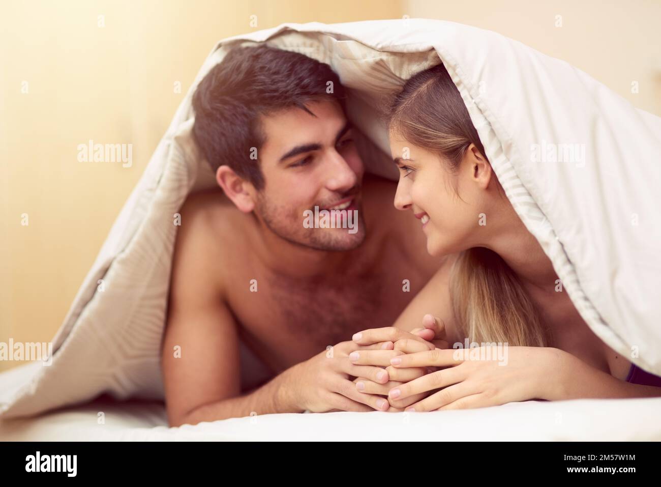 Sie sprechen mit ihren Augen. Ein liebevolles junges Paar, das sich anlächelt, während es unter einer Decke liegt. Stockfoto