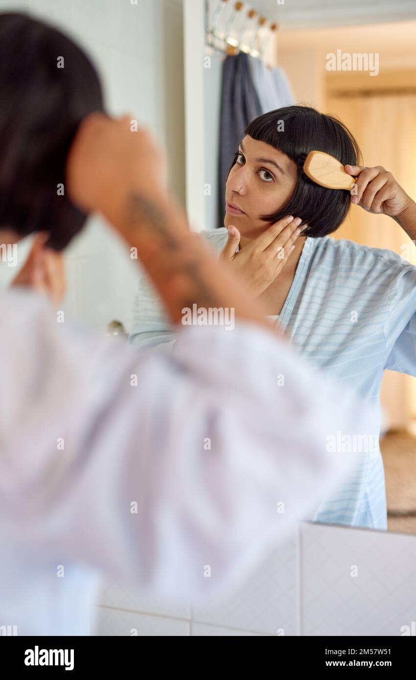 Kein Kabelgewirr. Eine junge Frau im Bademantel, die sich morgens im Badezimmerspiegel die Haare bürstet. Stockfoto