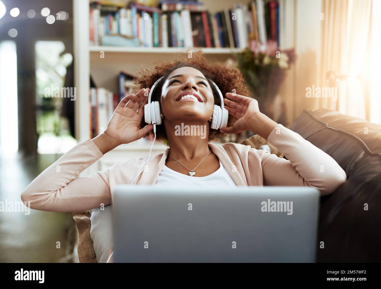 Musik, die sich leicht am Ohr anfühlt. Eine junge Frau, die sich auf dem Sofa entspannt und Musik auf ihrem Laptop hört. Stockfoto
