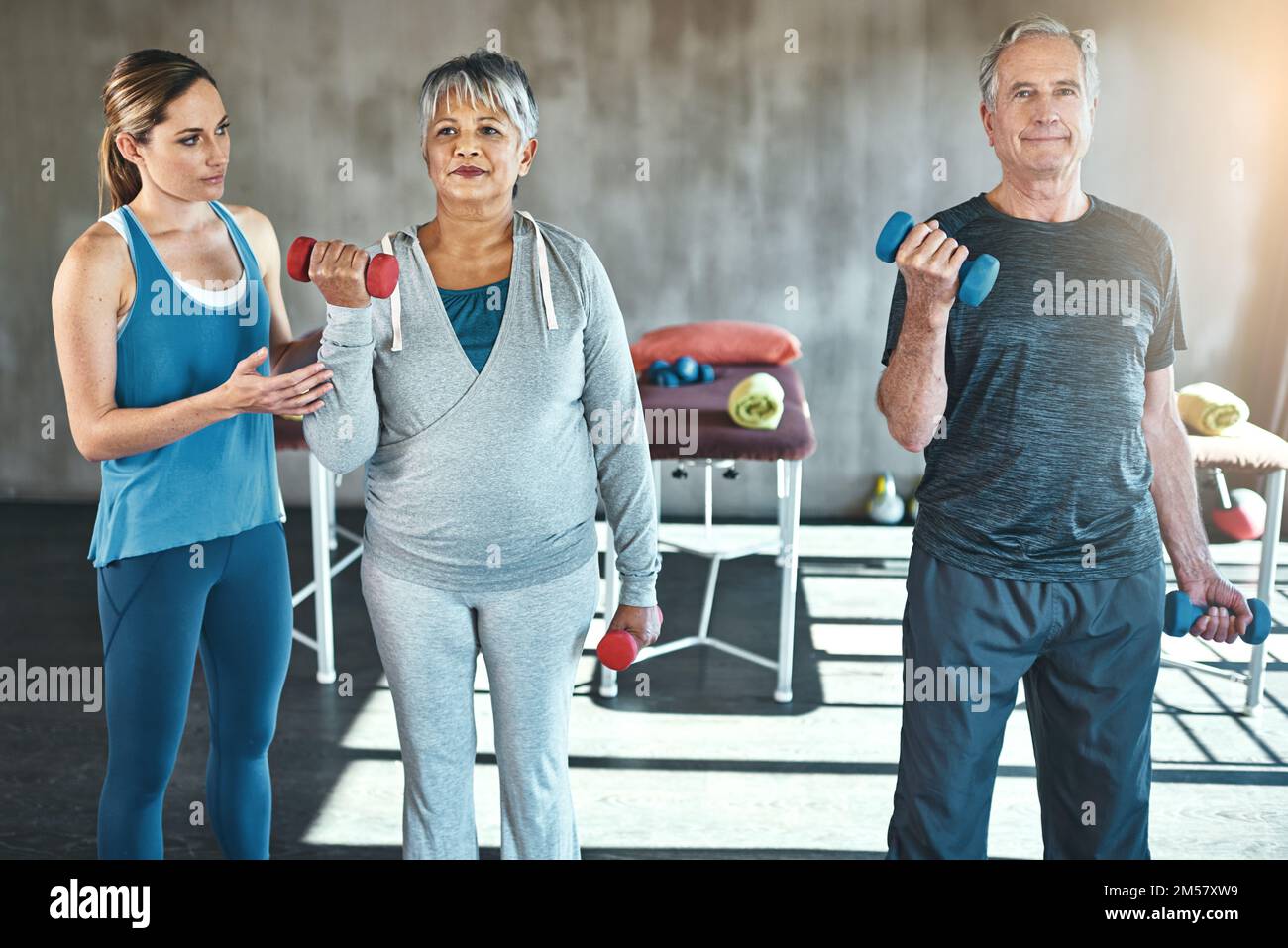 Gute Gesundheit ist ein lohnender Ruhestand. Ein älterer Mann und eine ältere Frau, die mit Hilfe eines Physiotherapeuten Gewichte benutzt. Stockfoto