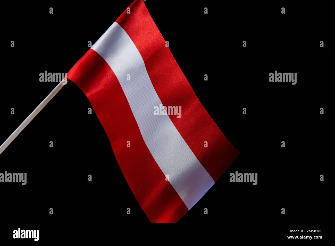 Die lettische Flagge auf schwarzem Hintergrund entwickelt sich und fliegt im Wind Stockfoto