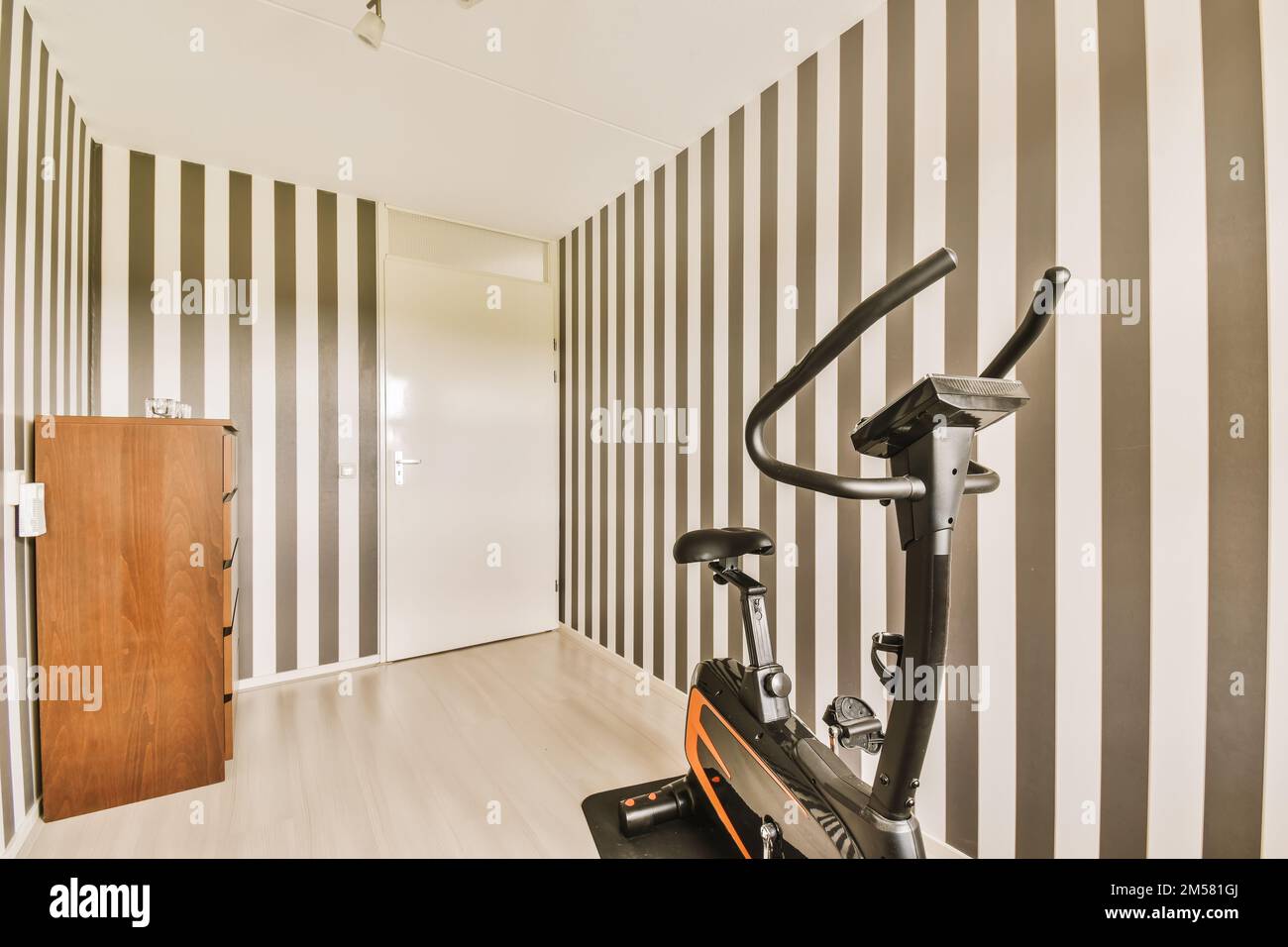 Ein Fitnessraum mit einem Heimtrainer auf dem Boden und schwarz-weiß gestreiften Tapeten an den Wänden Stockfoto