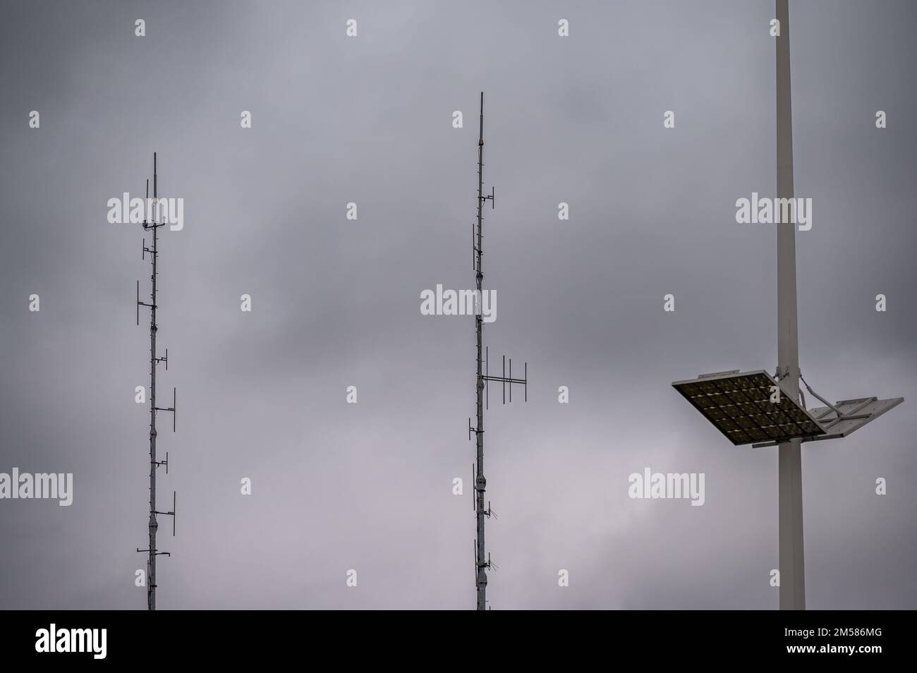 Kurzwellenantennen und LED-Einbauleuchte für den Außenbereich an großen Masten gegen graue Wolken Stockfoto