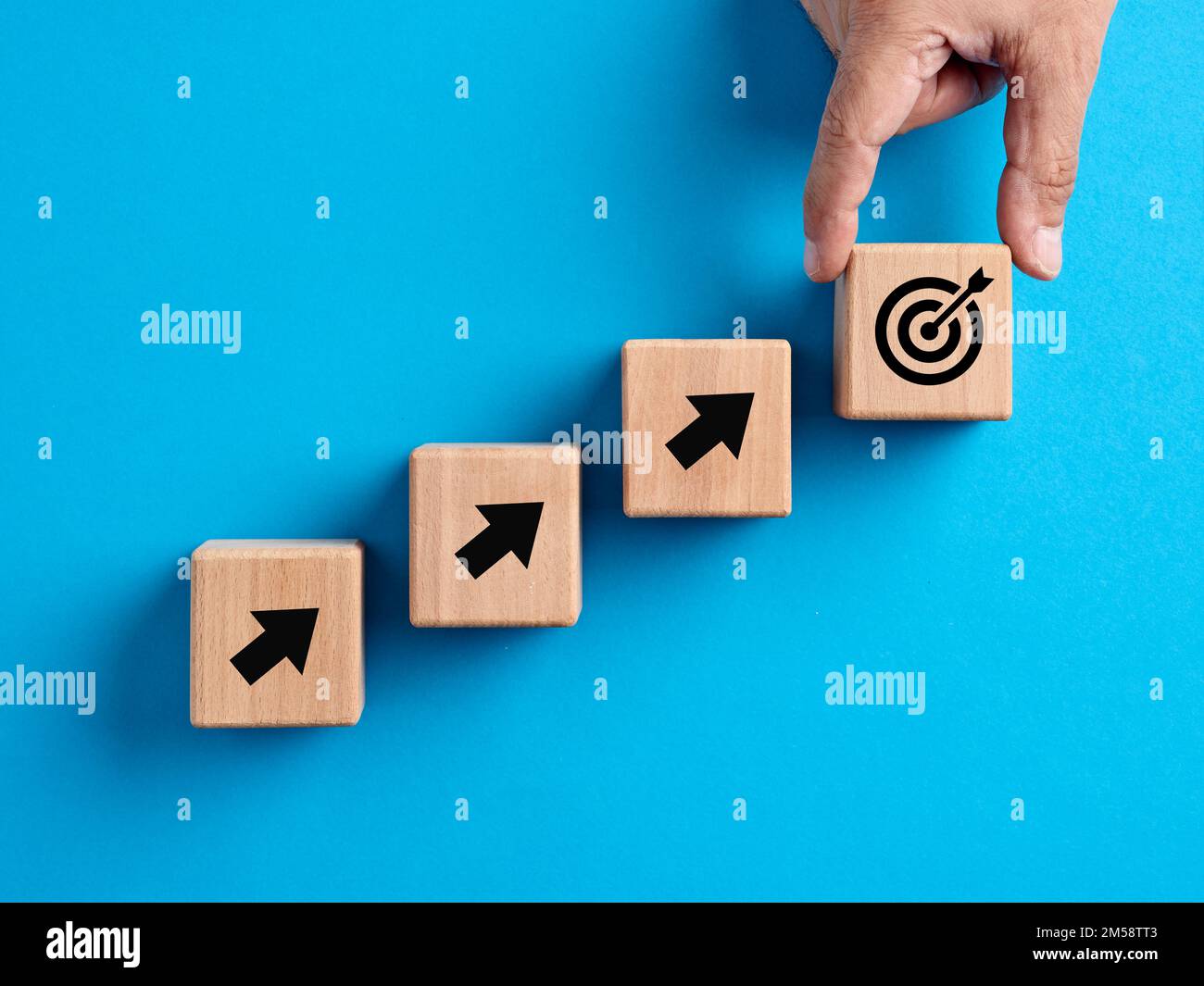 Zielerreichung, Zielsetzung, Geschäftsziele, Wachstums- und Erfolgskonzepte. Die Hand platziert einen Holzwürfel mit dem Zielsymbol. Stockfoto