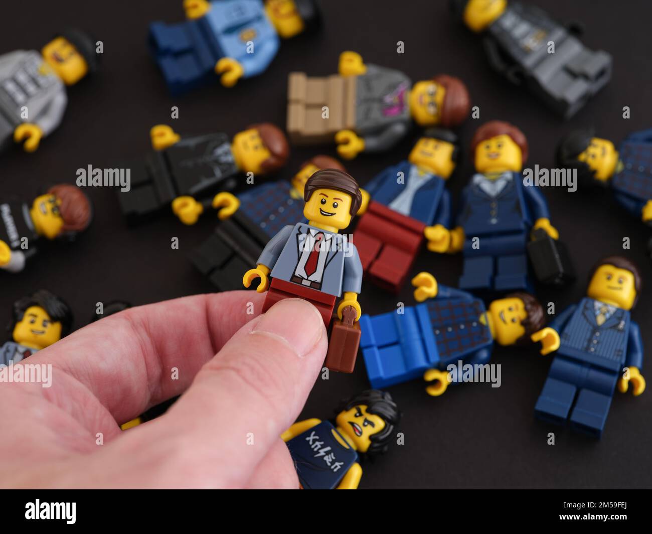 Tambov, Russische Föderation - 09. Oktober 2022 Eine Hand, die eine Lego-Geschäftsmann-Minifigure gegen einen Haufen Minifiguren hält, die auf einem schwarzen Ba liegen Stockfoto