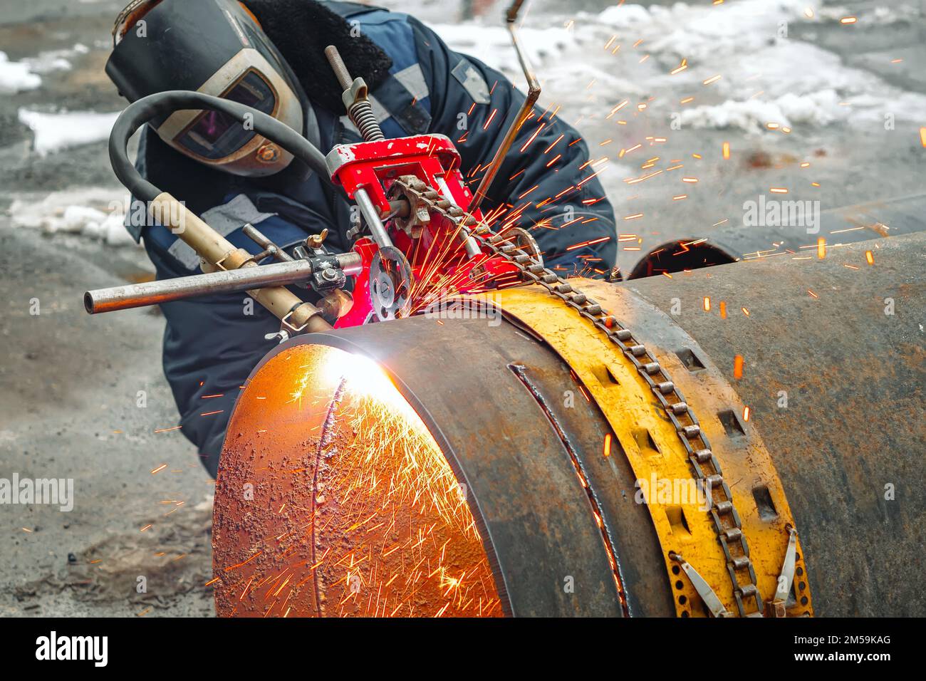 Funktionierender Schweißer schneidet Metall und Funken fliegen. Gasschneiden von grossen Rohrdurchmessern mit Acetylen und Sauerstoff. Industrielle Metallzerspanung in der Öl- und Gasindustrie. Stockfoto