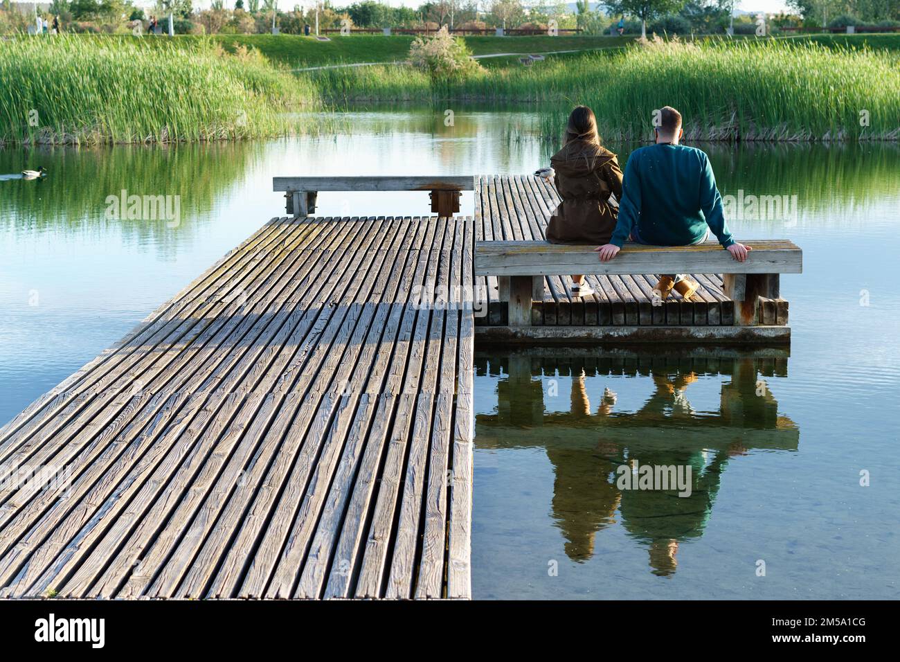 Ein junges Paar, das auf einer Bank auf einem See-Ponton sitzt und den Sonnenaufgang beobachtet Stockfoto