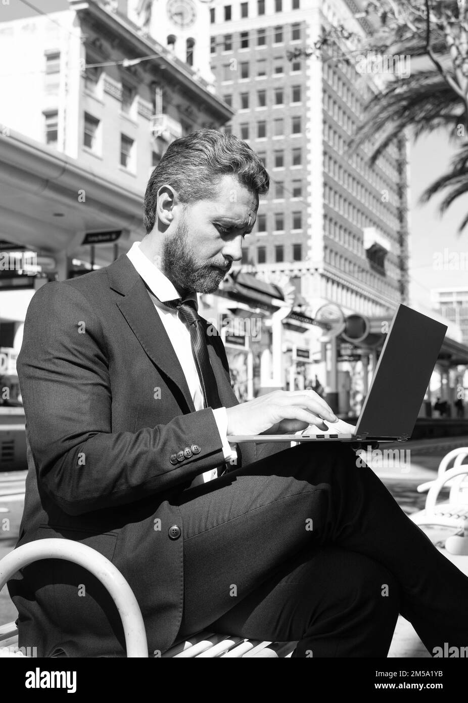 Reifer Mann Geschäftsmann in Anzug sitzen auf der Bank in Outdoor-Stadt arbeiten online auf Laptop, agile Geschäft Stockfoto