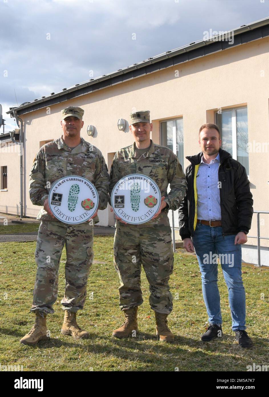 USAG Wiesbaden Commander Oberst Mario Washington präsentiert dem Hauptquartier und dem Hauptquartier-Bataillon in den USA die Schilder zum Green Boot-Programm Army Europe-Africa, Kommandoleiter des Bataillons, Major Joseph Daniel, zusammen mit Tomasz Filatow, Energy Manager bei der Direktion für öffentliche Arbeiten der Garrison. Stockfoto