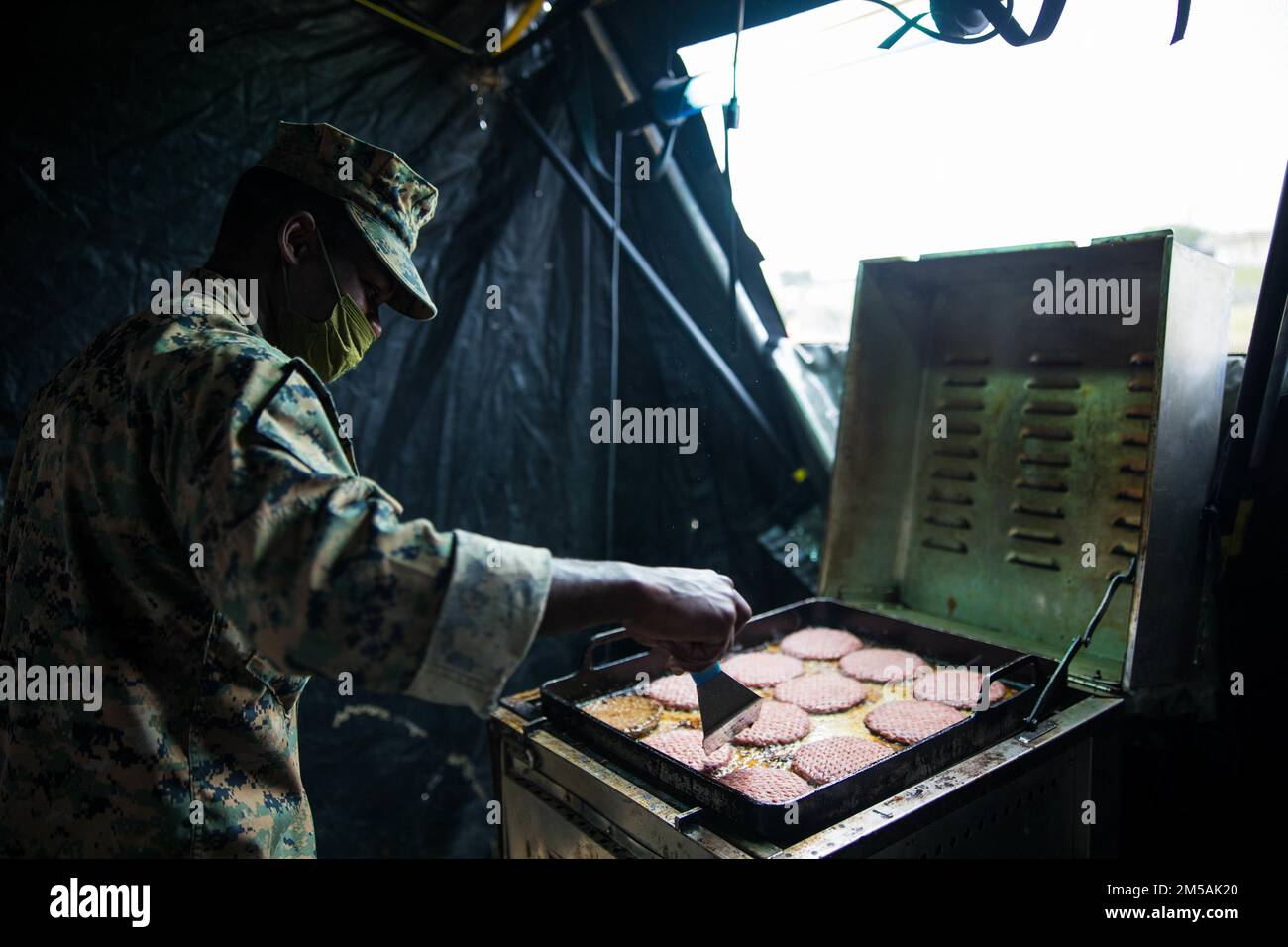 USA Marinekorps Lance CPL. Valfried Sokpoli, ein Spezialist für Lebensmitteldienstleistungen mit der Marinekorps-Unterstützungseinheit (MWSS) 172, 1. Marine Aircraft Wing, kocht Burger während der Jungle Warfare Übung (JWX 22) in der Marine Corps Air Station Futenma, Okinawa, Japan, 16. Februar 2022. JWX 22 ist eine groß angelegte Übung vor Ort, die darauf ausgerichtet ist, die integrierten Fähigkeiten gemeinsamer und verbundener Partner zu nutzen, um das Bewusstsein für alle Bereiche, Manöver und Brände in einer verteilten maritimen Umgebung zu stärken. Stockfoto