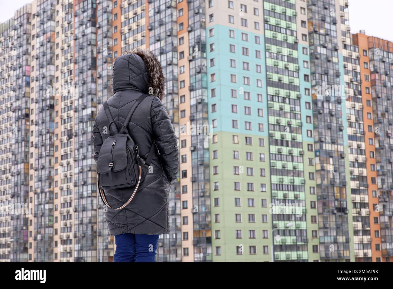 Neues Wohnviertel in der Stadt, Frau in schwarzem Ledermantel, die auf dem Hintergrund eines Wohngebäudes steht. Immobilien, Wohnung oder Miete wählen Stockfoto