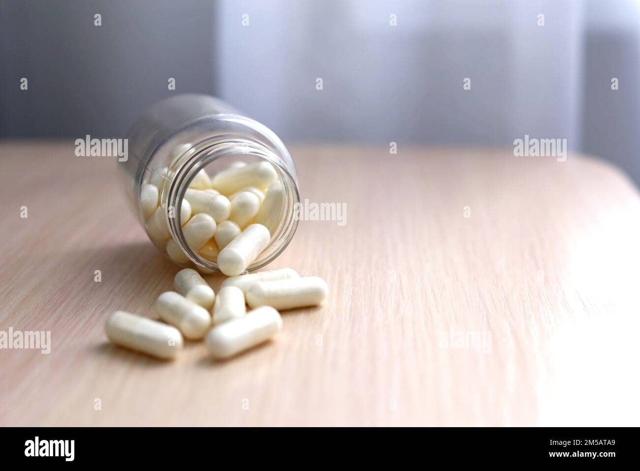 Weiße Pillen auf einem hellen Holztisch, Medikamente in Kapseln aus einer Flasche verstreut. Hintergrund für Pharmazie, Antibiotika, Vitamine Stockfoto