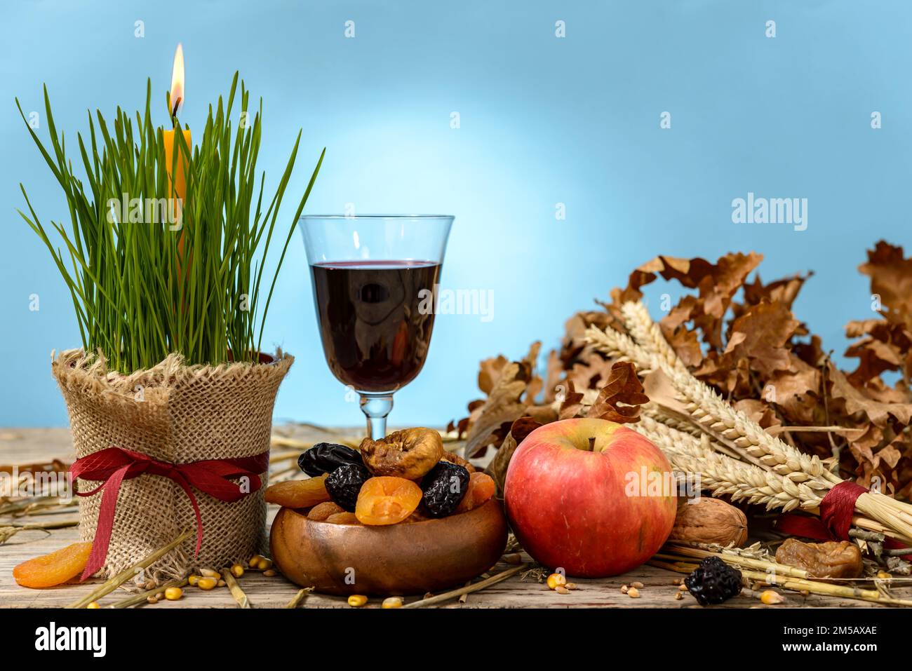 Yule log oder badnjak, Apfel, Wein, Getreide, getrocknete Früchte und eine brennende Kerze in grünem Weizen auf einem Holztisch. Konzept Feier orthodoxen Weihnachten. Stockfoto