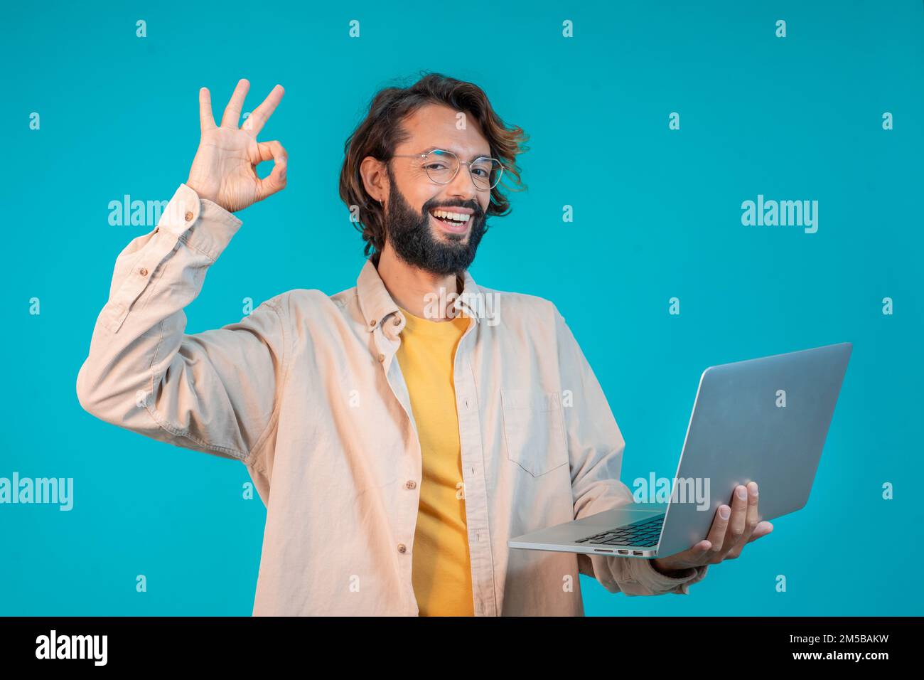 Porträt eines Mannes, der einen Laptop in der Hand hält und den Erfolg isoliert vor blauem Hintergrund feiert Stockfoto