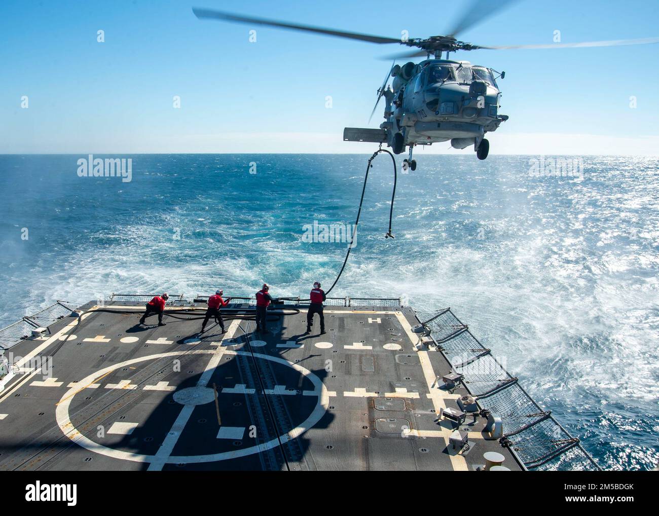 220219-N-EH998-1129 ATLANTISCHER OZEAN (19. Februar 2022) Seeleute an Bord des Guided-Missile Destroyers USS Farragut (DDG 99) betanken während des Fluges mit einem MH-60 Sea Hawk Helikopter, der am Helicopter Maritime Strike Squadron (HSM) 26 befestigt ist, während sie sich auf dem Weg zum Surface Warfare Advanced Tactical Training (SWATT) befinden. Farragut ist Teil der Destroyer Squadron (DESRON) 26, die die Carrier Strike Group (CSG) 10 unterstützt. SWATT wird vom Naval Surface and Mine Warfighting Development Center (SMWDC) geleitet und soll die Kampffähigkeit, die Letalität und die Interoperabilität der teilnehmenden Einheiten verbessern. Stockfoto