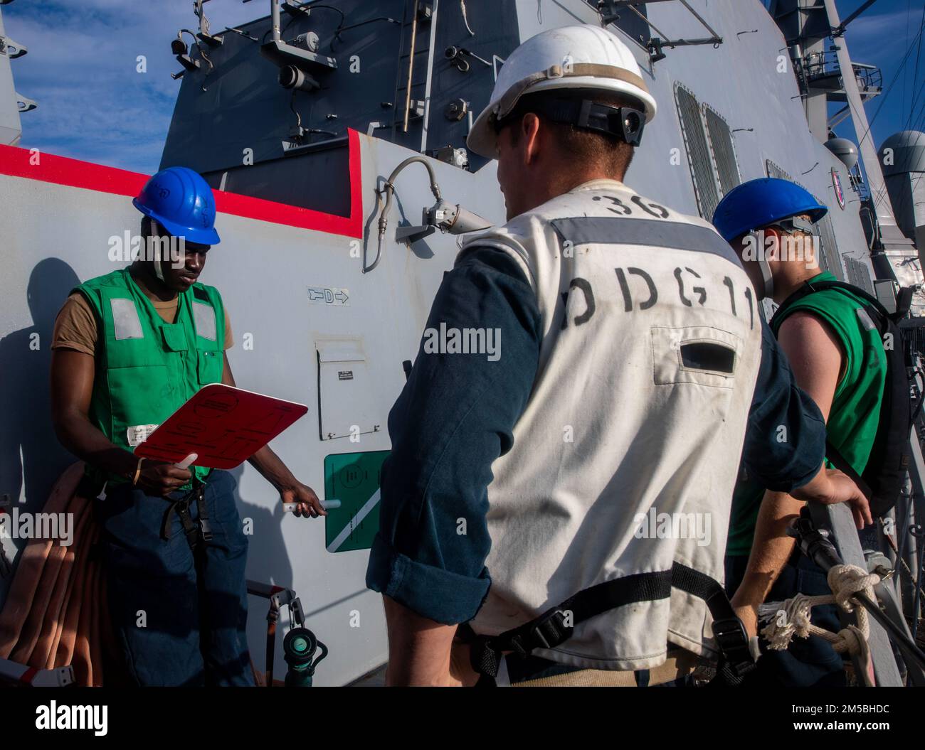 SÜDCHINESISCHES MEER (22. Februar 2022) Chief Boatswain's Mate Matthew Klimek aus Yuba City, Kalifornien, lehrt Seaman Romario Clennon aus Atlanta, wie man dem Trockenfrachtschiff der Lewis- und Clark-Klasse USNS Carl Brasyer (T-AKE-7) in Vorbereitung auf eine Wiederauffüllung auf See an Bord einer von der Arleigh-Buralph-Johnson-Klasse geführten Raketenstörung signalisiert (DDG 114). Ralph Johnson ist der Task Force 71/Destroyer Squadron (DESRON) 15, dem größten nach vorn verlegten DESRON der Marine, und der Hauptstreitkraft der US-7.-Flotte zugewiesen. Stockfoto