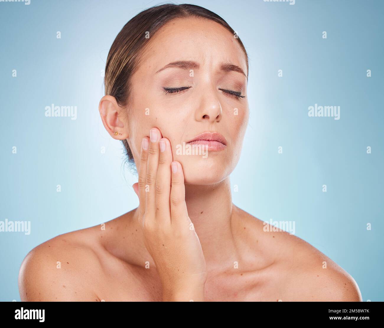 Zahnschmerzen, Zahnhygiene und Mundpflege mit einer Modellfrau, die ihr Gesicht vor Schmerzen auf blauem Hintergrund hält. Zahnarzt, Kavität und Mund mit einem attraktiven Stockfoto