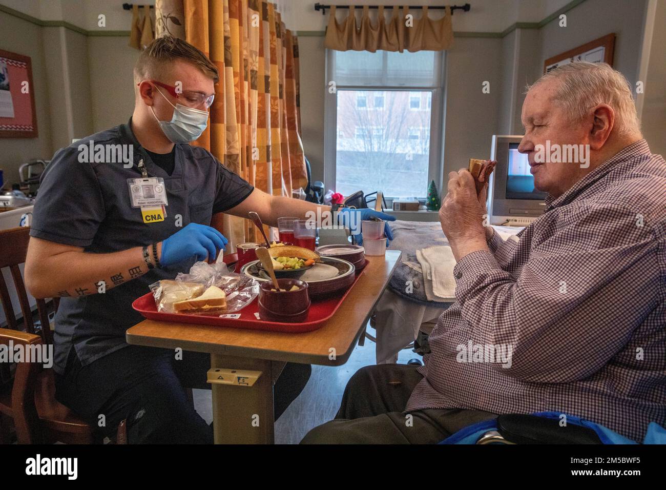 USA Army PFC. Robert D. VonScheven, Bravo Company, 104. Brigadeingenieurbataillon, 44. Infanterie-Brigaden-Kampfteam, New Jersey Army National Guard, assistiert Charles Riley, ein Bewohner des New Jersey Veterans Memorial Home in Vineland, mit seinem Mittagessen in Vineland, New Jersey, 24. Februar 2022. VonScheven betreut die Hausbewohner als zertifizierte Pflegehelferin. Mehr als 70 Soldaten der Nationalgarde und Flugzeuge von New Jersey sind zertifizierte Pflegehelfer und in den Bereichen Lebensmittel, Infektionskontrolle, Informationstechnologie, Lebenserweiterung, Logistik, Und COVID-19-Tests. (Neuer Jers Stockfoto