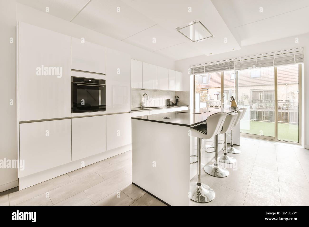 Eine moderne Küche mit weißen Schränken und Geräten im mittleren Teil des Zimmers, der zur Terrasse hin offen ist Stockfoto