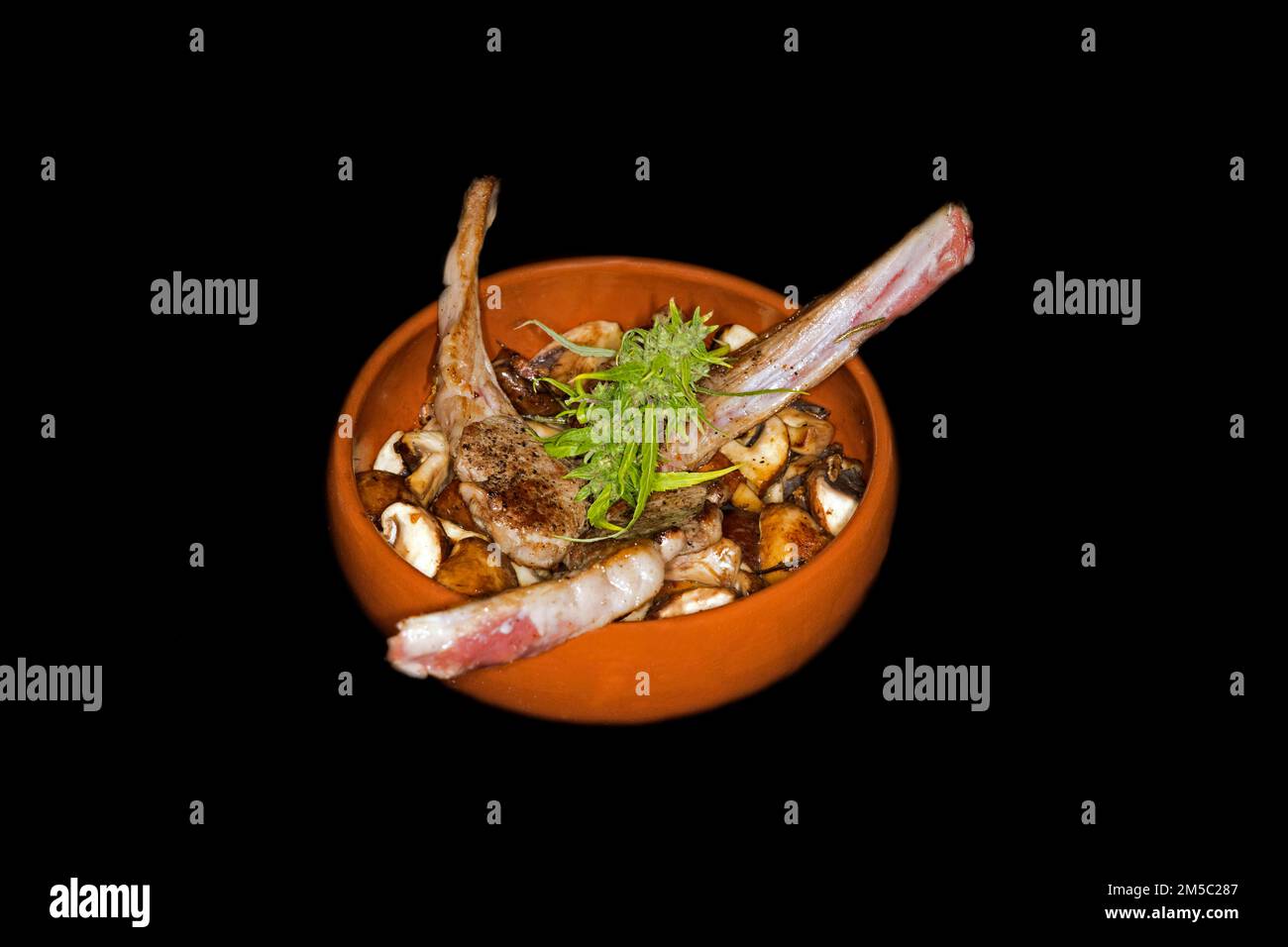 Drei gegrillte Lammkoteletts auf gerösteten Austernpilzen (Agaricus) (SYN. : Psalliota), in einer spanischen feuerfesten Keramikschüssel (Cazuela), Lebensmittelfotografie Stockfoto