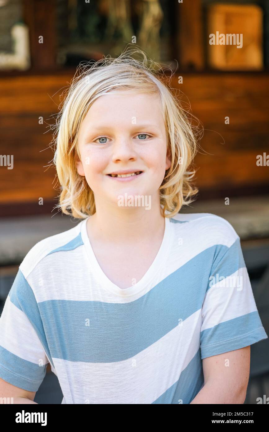 Ein Junge mit frischem Gesicht, fröhlichem Lächeln und langen blonden Haaren, im Sommer draußen Stockfoto