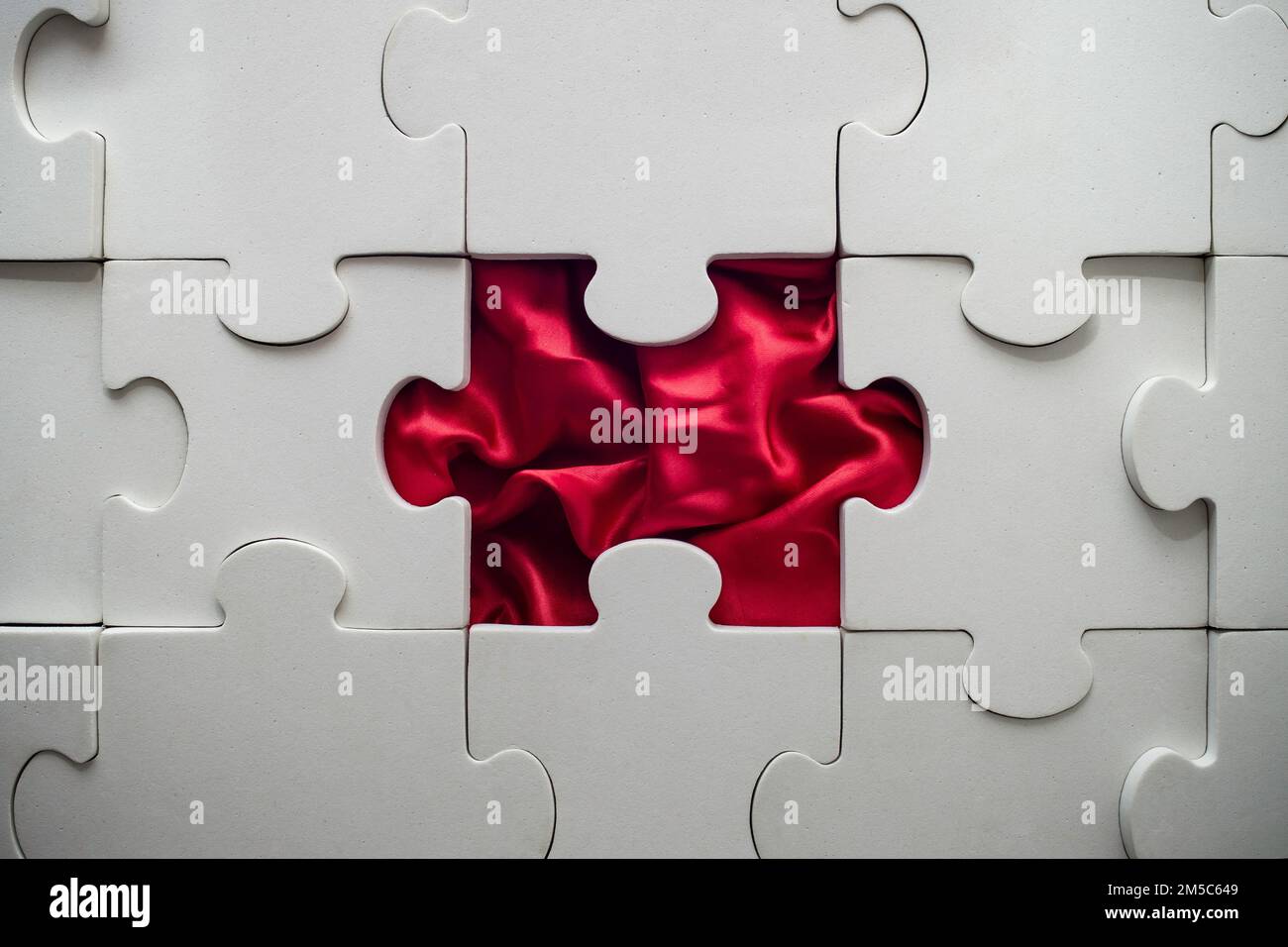 Weißes Puzzle mit fehlendem Teil und roter Satin Stockfoto