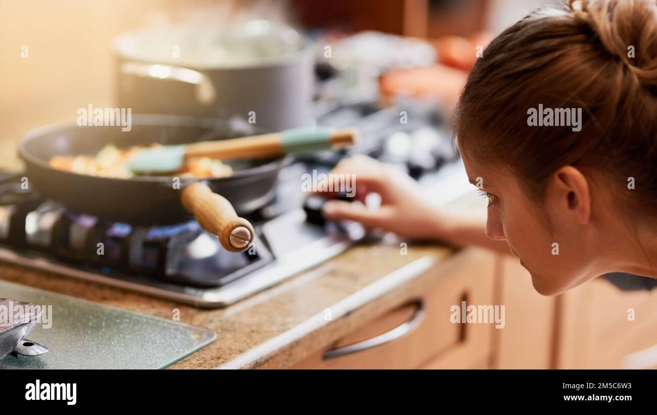 Ein Auge zu haben, damit sie das Essen nicht verbrennt. Eine junge Frau, die zu Hause eine Mahlzeit zubereitet. Stockfoto