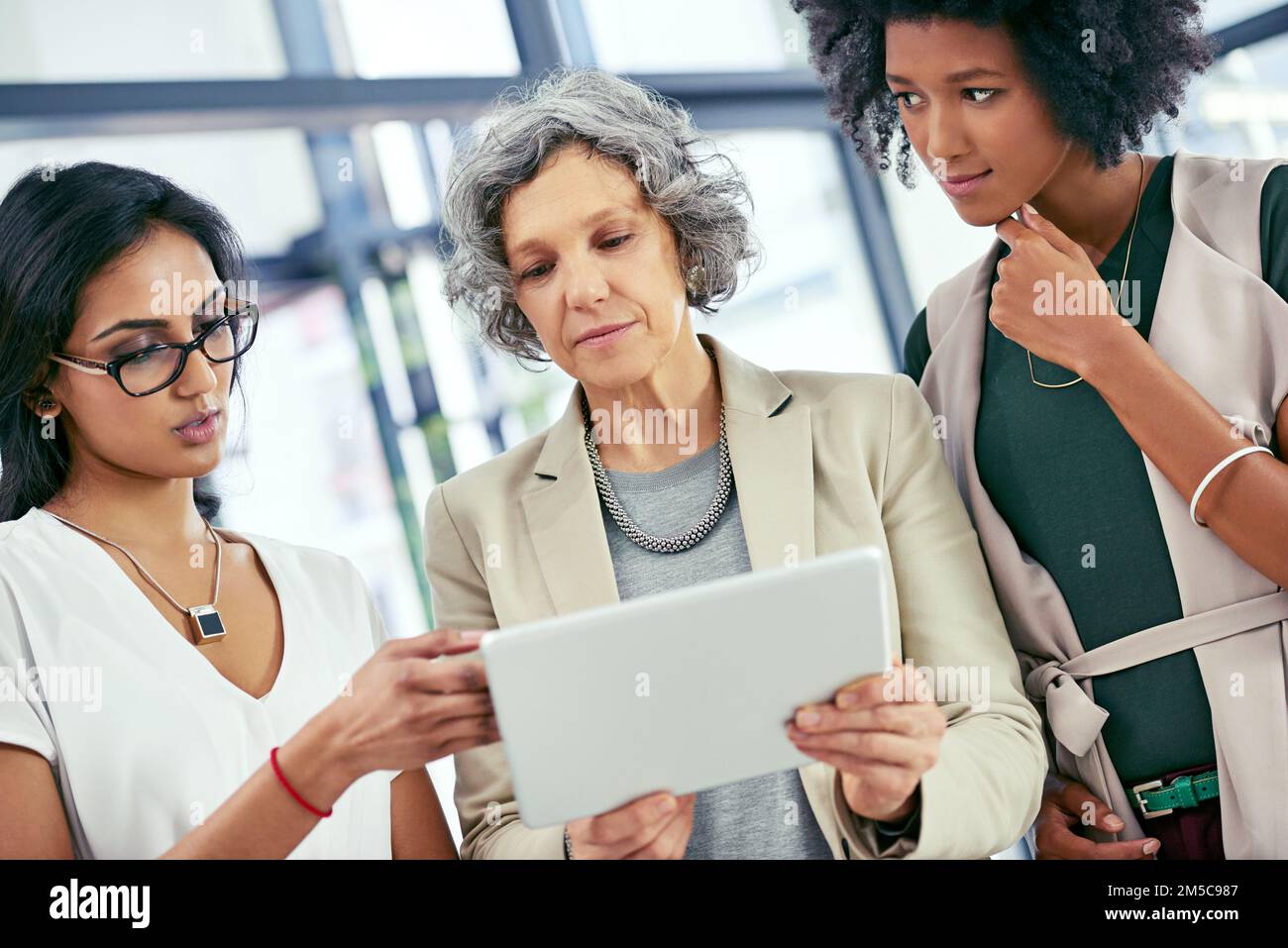 Ihre vielfältigen Beiträge helfen ihnen, Dinge anders zu betrachten. Ein Team von Kollegen, die während eines informellen Meetings ein digitales Tablet verwenden. Stockfoto