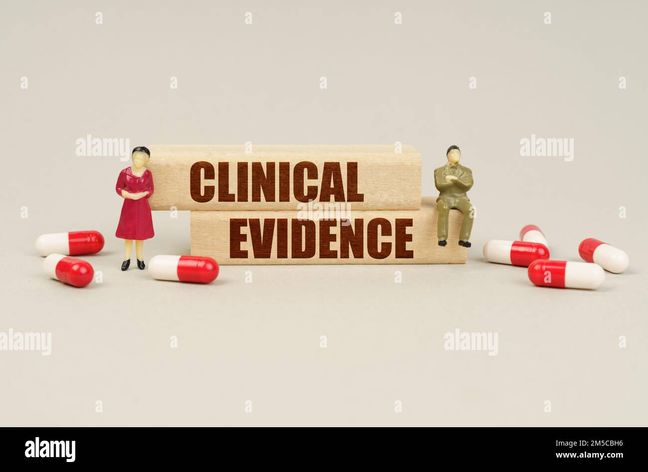 Medizinisches Konzept. Neben den Miniaturfiguren von Menschen sind Tabletten und Holzblöcke mit der Inschrift - Klinische Evidenz Stockfoto