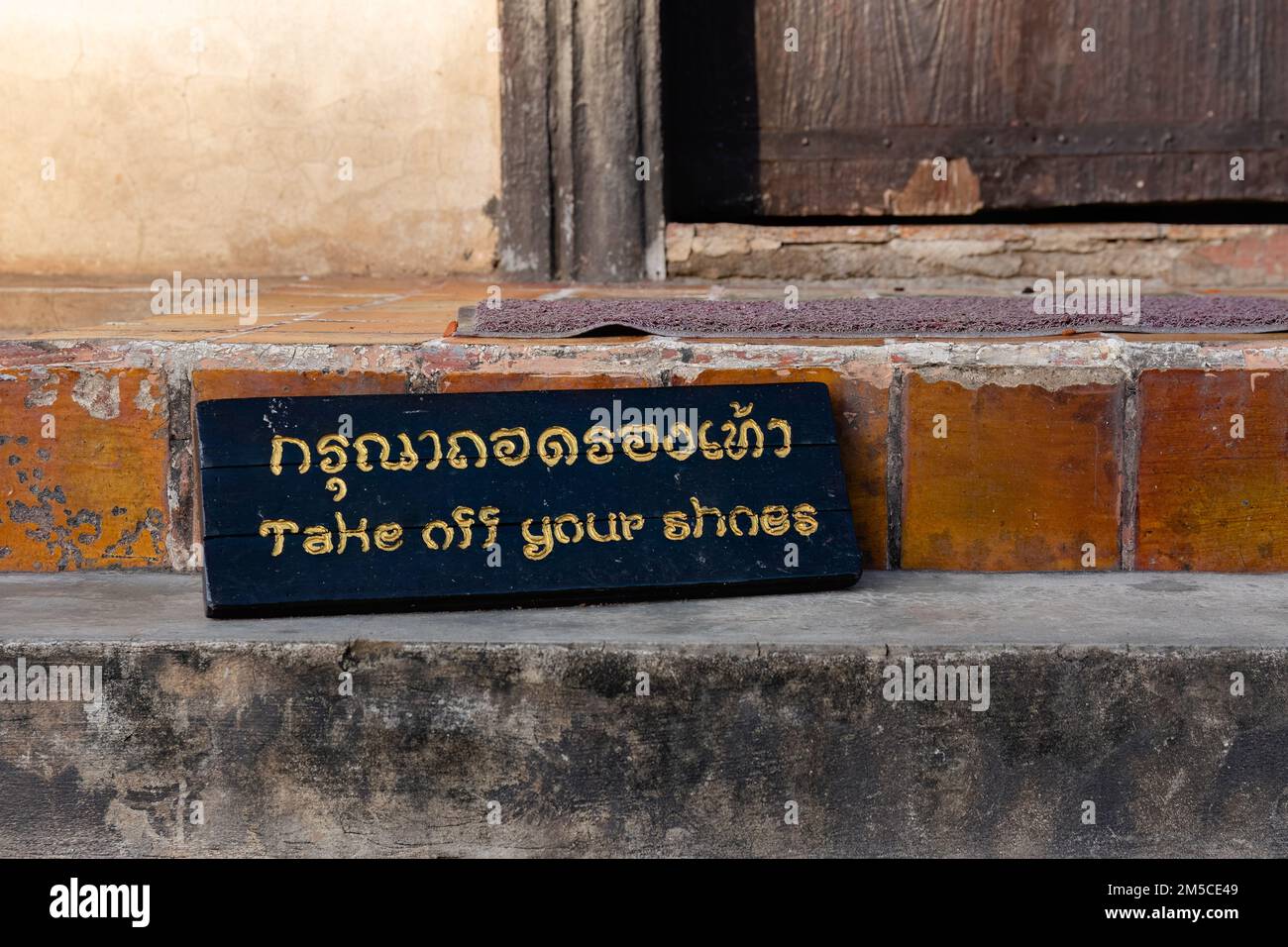 Schild mit der Aufschrift: Ziehen Sie Ihre Schuhe auf Englisch und Thailändisch am Eingang zum Tempel aus Stockfoto