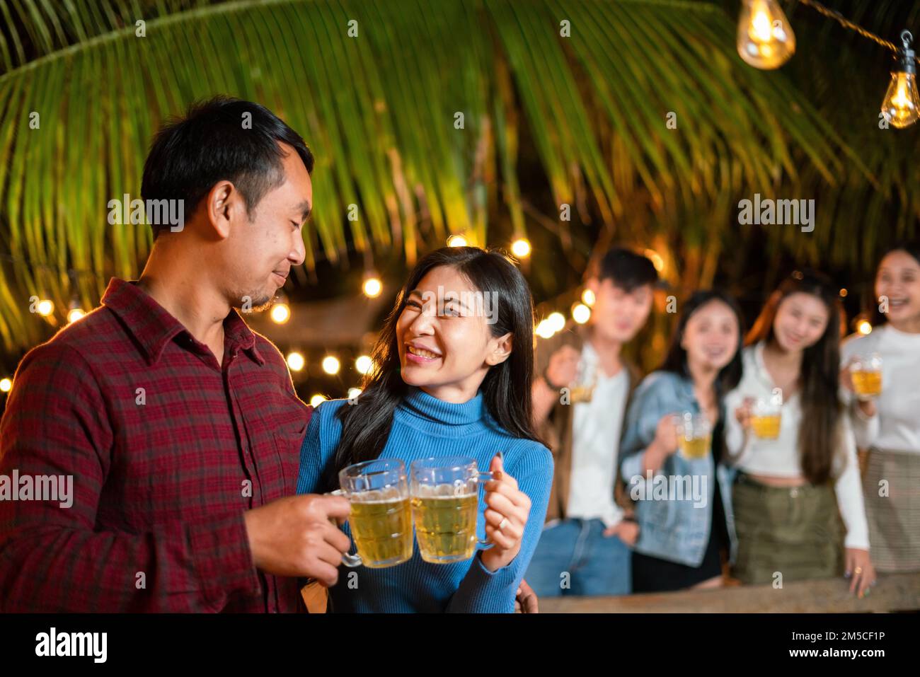 Glückliches, junges asiatisches Paar, das eine Party mit Freunden feiert, während es Bier trinkt. Stockfoto