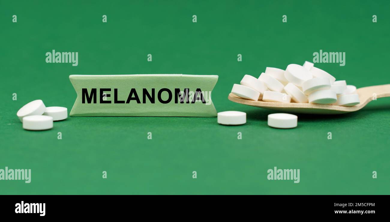 Medizinisches Konzept. Auf einer grünen Oberfläche, ein Holzlöffel mit Pillen und ein Schild mit der Inschrift - MELANOM Stockfoto