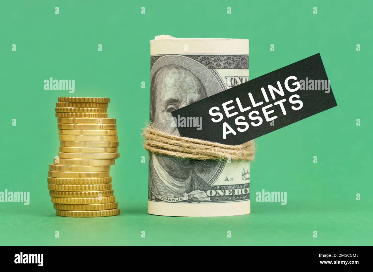 Geschäftskonzept. Auf einer grünen Oberfläche befinden sich Münzen und Dollar in einem Bündel. Auf dem Dollarzeichen mit der Aufschrift "Selling Assets" Stockfoto