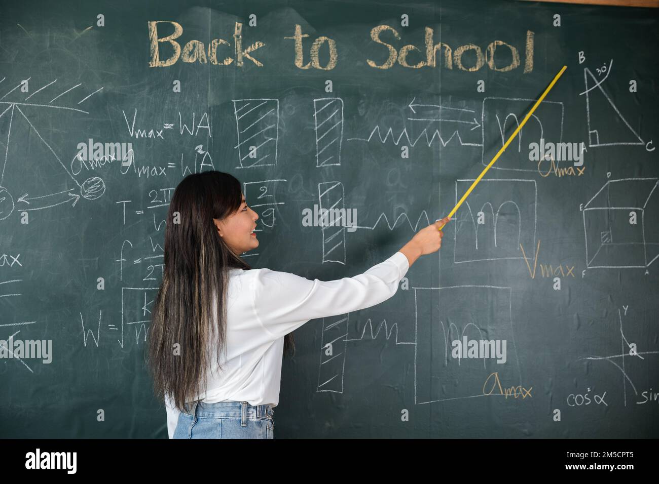 Asiatische Lehrerin lächelt mit Holzstab, der auf die Tafel zeigt Stockfoto