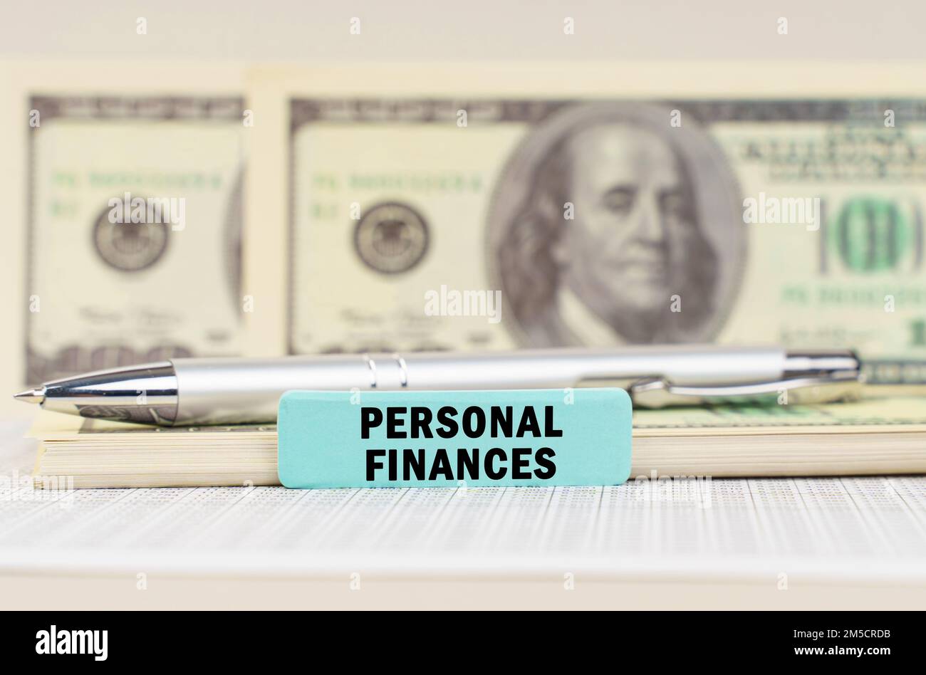 Geschäftskonzept. Auf den Dollars sind ein Stift und ein Schild mit der Aufschrift "Persönliche Finanzen". Im Hintergrund in einem verschwommenen Hintergrund sind Dollar Stockfoto