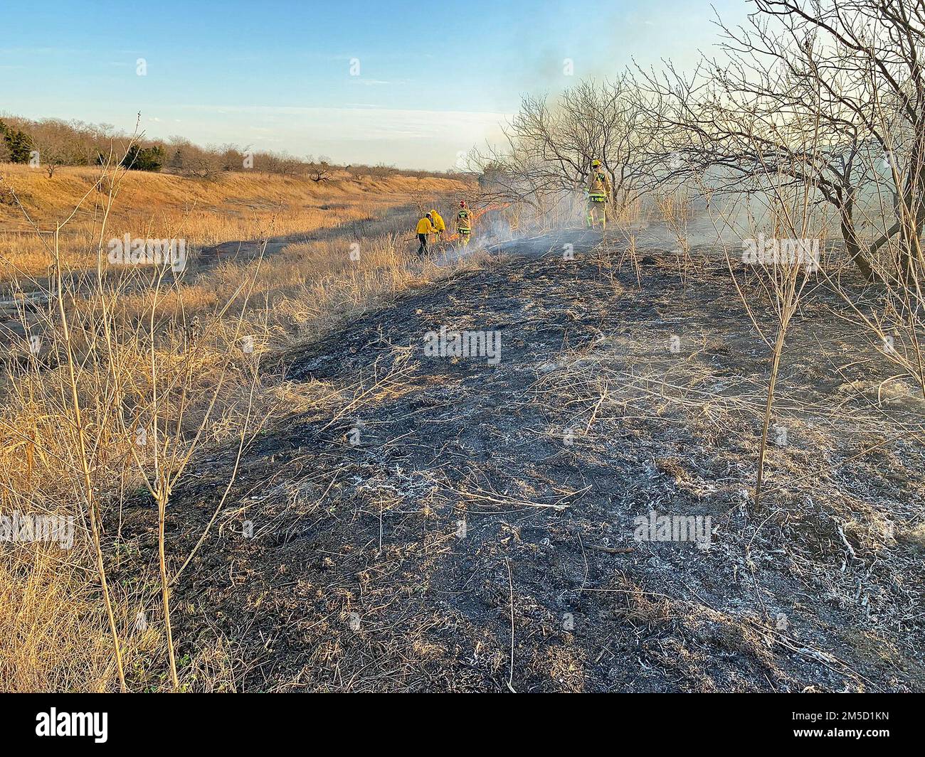 LEWISVILLE, Texas (2. März 2022) Feuerwehrleute und Partneragenturen kämpfen unter dem Lewisville Lake Dam gegen eine brennende Graslandfläche. Im Lewisville Lake Environmental Learning Area am Lewisville Lake wurde ein vorgeschriebenes Feuer ausgelöst, um Prärien unterhalb des Lewisville Dam zu erschaffen, wiederherzustellen und zu beleben. Man ging davon aus, dass dieser Brand vor 12 Uhr unter Kontrolle gebracht werden sollte, aber aufgrund von Wind- und Wetterveränderungen konnte der Brand aus dem vorgesehenen Bereich entweichen. Feuerwehrleute aus Flower Mound, Frisco und mehreren anderen umliegenden Städten reagierten auf gegenseitige Hilfeanfragen mit Bürstenwagen, um Conta zu helfen Stockfoto