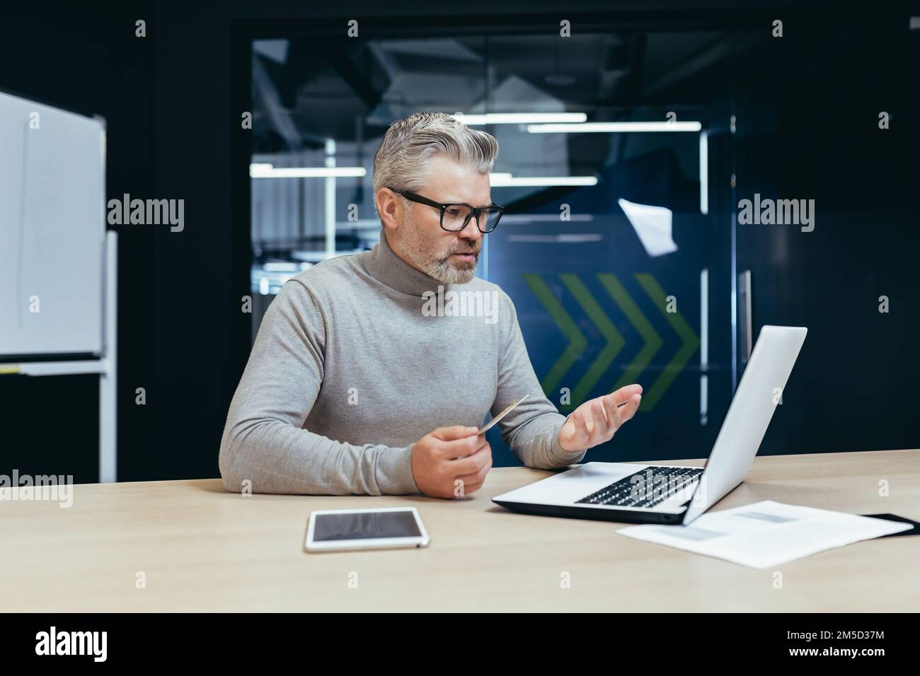 Der grauhaarige Geschäftsmann im Büro war frustriert und traurig, als er im Online-Shop Banktransaktionen und Einkäufe tätigte, ein Mann, der eine Kreditkarte hatte und ein Notebook benutzte. Stockfoto