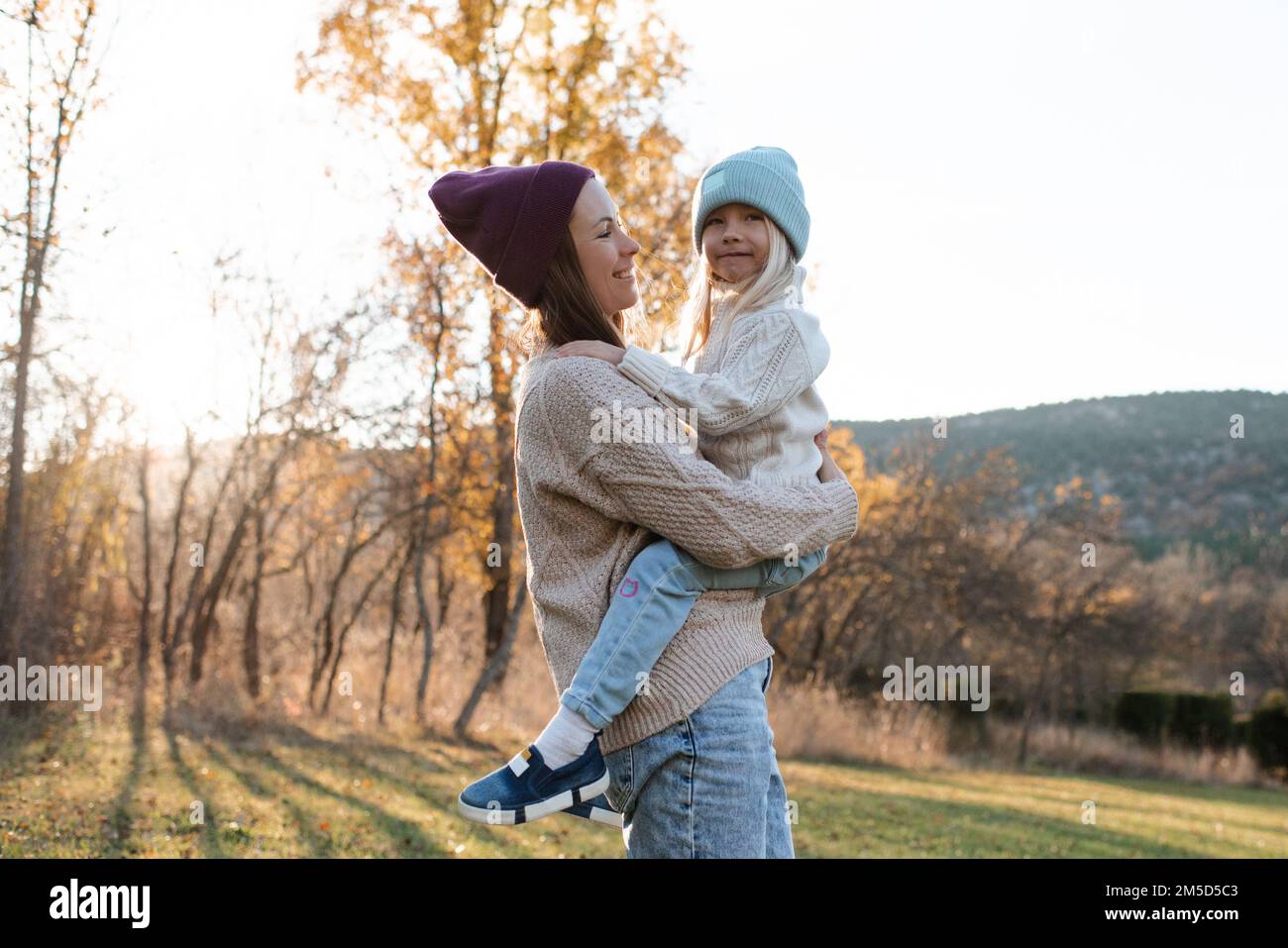 Eine lächelnde glückliche Mutter hält ein kleines Mädchen und trägt im Herbstpark im Freien lässige Kleidung. Familieninhalte. Mutterschaft. Stockfoto