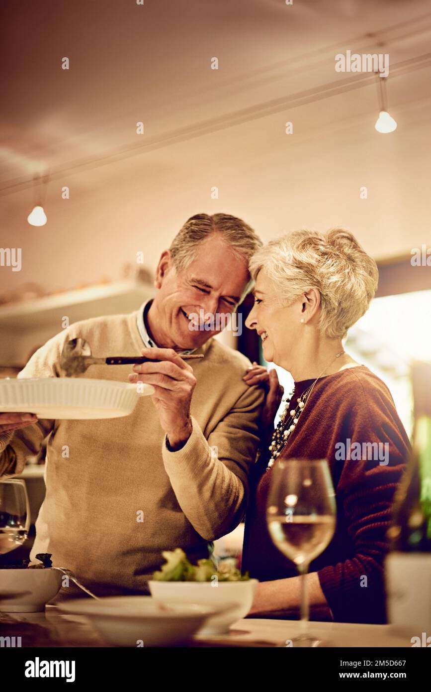 Es ist dein Lieblingsessen, Schatz. Ein älteres Ehepaar, das zu Hause in der Küche eine Mahlzeit zubereitete. Stockfoto