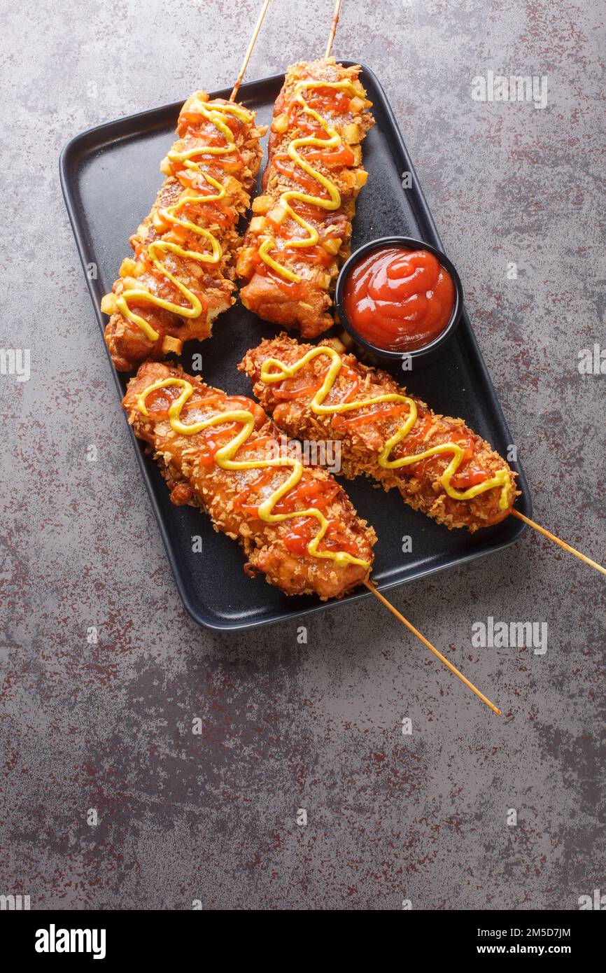 Koreanische Maishunde werden aus Wurst, Mozzarella-Käse auf Spieß hergestellt und in süßen Mehlteig überzogen, bevor sie in eine Schicht Closeu-Garnierung Rollen Stockfoto