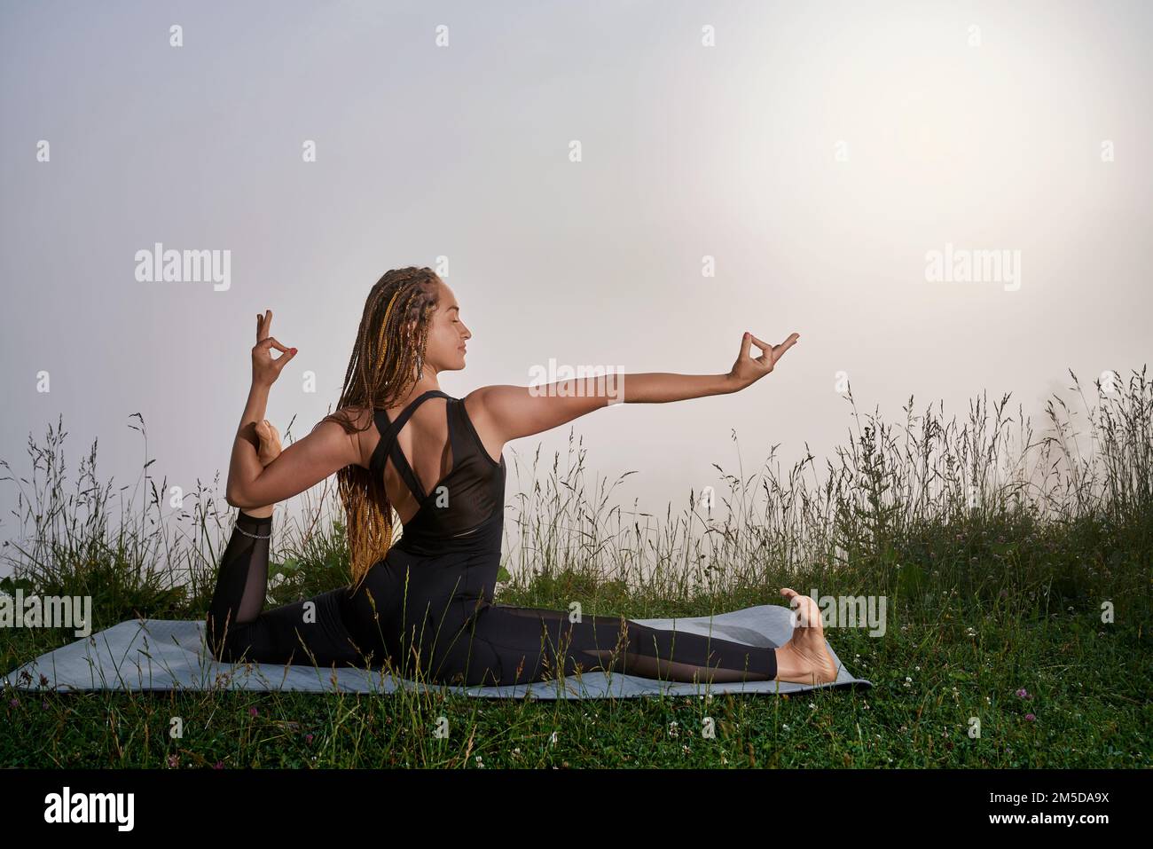 Fitness-junge Frau mit langer geflochtener Frisur, die Yoga in den Morgenbergen praktiziert. Konzentrierungs- und Meditationsbegriff. Stockfoto