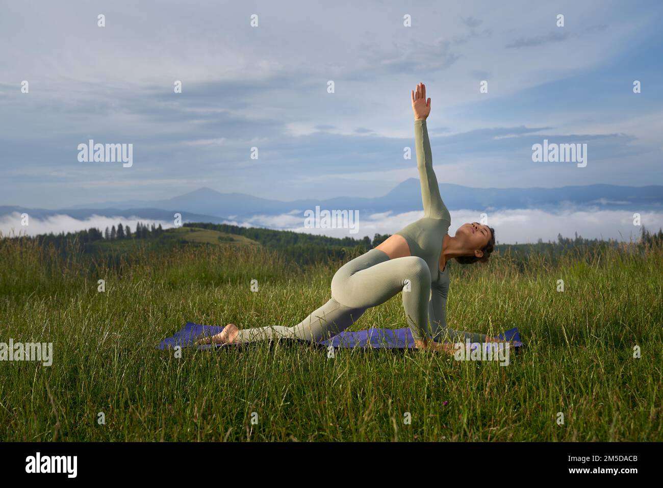 Flexible junge Frau in grüner Sportkleidung, die morgens im Freien trainiert. Eine ziemlich schlanke Dame, die Yoga-Übungen an der frischen Luft in den Bergen genießt. Stockfoto