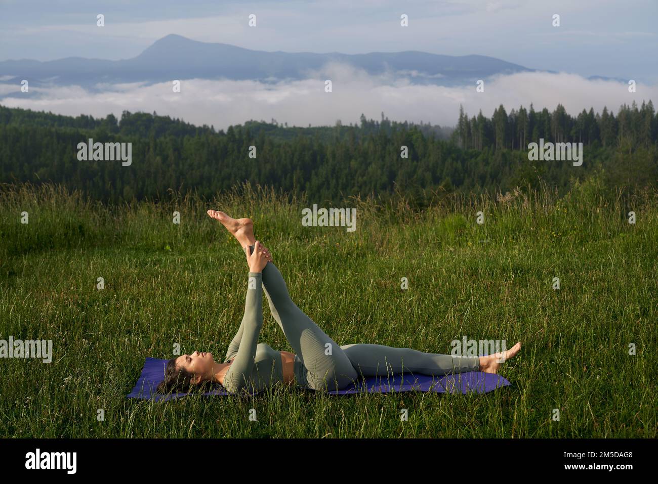 Junge sportliche Frau, die Yoga-Training in den grünen Sommerbergen genießt. Gleichgewicht zwischen körperlicher und mentaler Entwicklung. Gesunder Lebensstil. Stockfoto